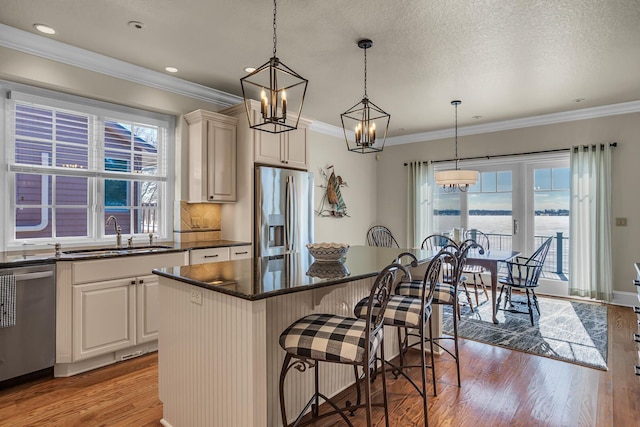 kitchen with decorative light fixtures, light wood-style flooring, appliances with stainless steel finishes, a sink, and a kitchen island