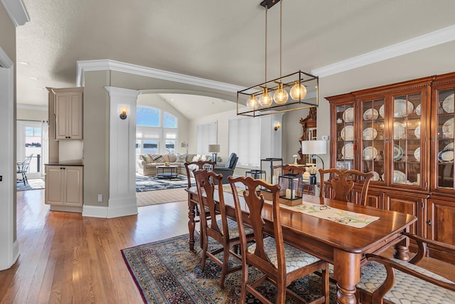 dining area featuring baseboards, arched walkways, lofted ceiling, crown molding, and light wood-type flooring