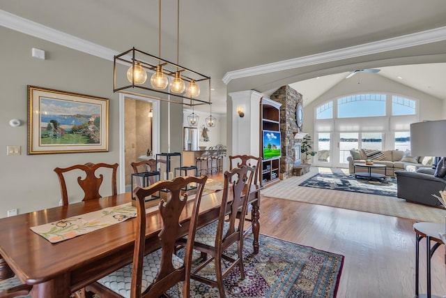 dining space with a stone fireplace, vaulted ceiling, crown molding, and wood finished floors