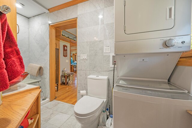 21598 Sylvan Rd, Reed City, MI 49677 - bathroom with stacked washer and clothes dryer, tile walls, toilet, a shower stall, and marble look tiles