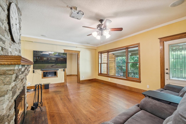 living room featuring a stone fireplace, crown molding, ceiling fan, and a textured ceiling