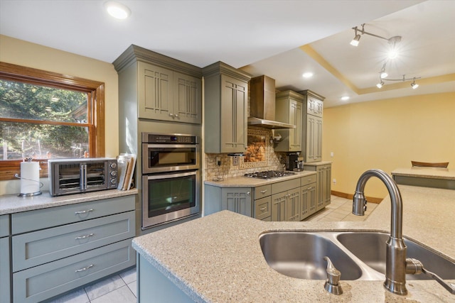 kitchen featuring backsplash, stainless steel appliances, sink, wall chimney range hood, and light tile patterned floors