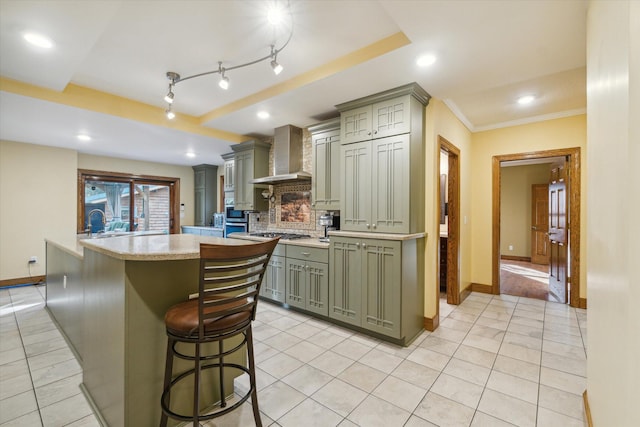 kitchen featuring wall chimney exhaust hood, backsplash, crown molding, a breakfast bar, and light tile patterned floors