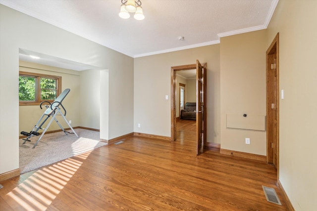 spare room with hardwood / wood-style floors, a chandelier, a textured ceiling, and ornamental molding