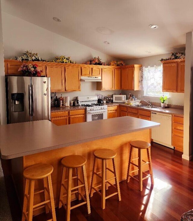 kitchen with a center island, dark hardwood / wood-style flooring, lofted ceiling, white appliances, and a kitchen bar