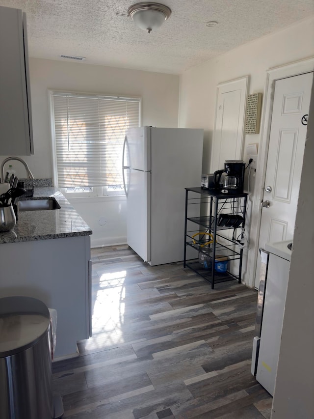 kitchen featuring light stone countertops, a textured ceiling, dark wood-type flooring, sink, and white refrigerator