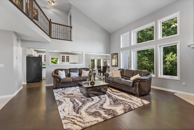 living room with a towering ceiling, a wealth of natural light, and dark wood-type flooring