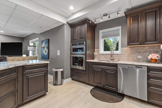 kitchen featuring appliances with stainless steel finishes, tasteful backsplash, dark brown cabinets, sink, and light hardwood / wood-style flooring