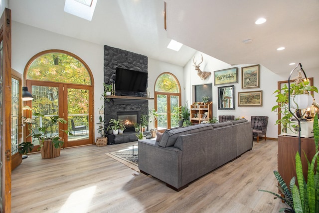 living room with vaulted ceiling with skylight, french doors, a fireplace, and light hardwood / wood-style flooring