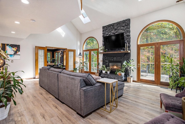 living room with french doors, a skylight, high vaulted ceiling, light hardwood / wood-style flooring, and a fireplace