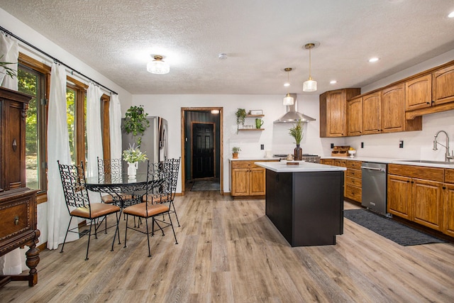 kitchen with wall chimney exhaust hood, sink, a center island, light hardwood / wood-style floors, and hanging light fixtures