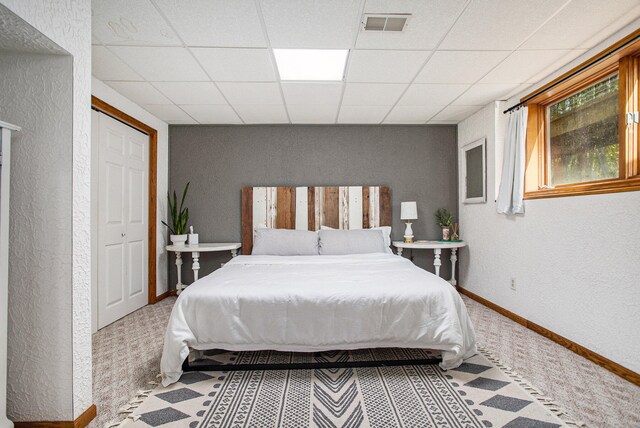 carpeted bedroom with a paneled ceiling and a closet