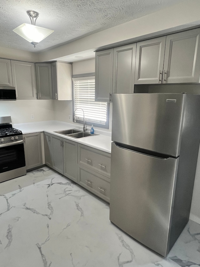 kitchen with gray cabinetry, sink, stainless steel appliances, and a textured ceiling