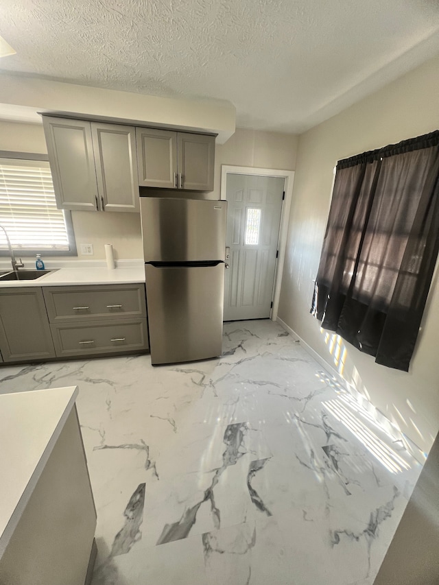 kitchen with a textured ceiling, stainless steel refrigerator, gray cabinetry, and sink