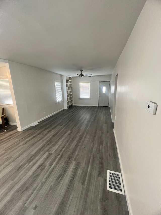 unfurnished living room featuring built in shelves, ceiling fan, and dark wood-type flooring