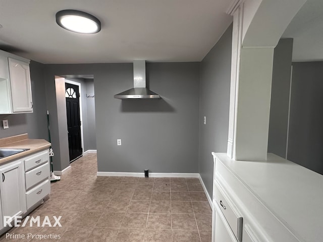 kitchen featuring white cabinets, light tile patterned floors, sink, and wall chimney range hood