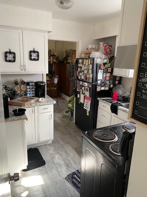 kitchen with black refrigerator, white cabinetry, light hardwood / wood-style flooring, and range with electric stovetop