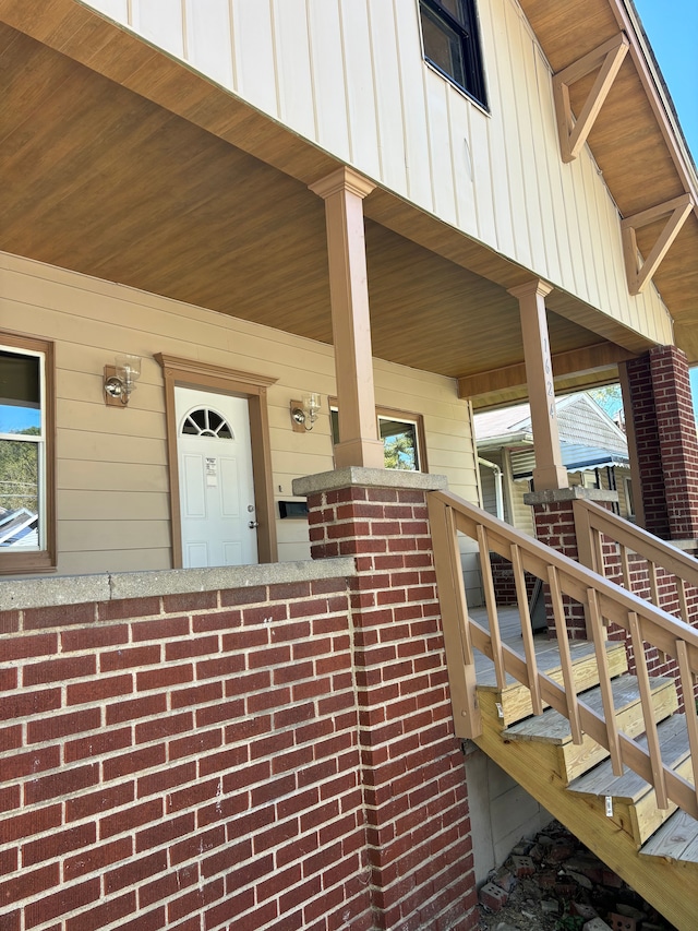 entrance to property with covered porch, brick siding, and board and batten siding