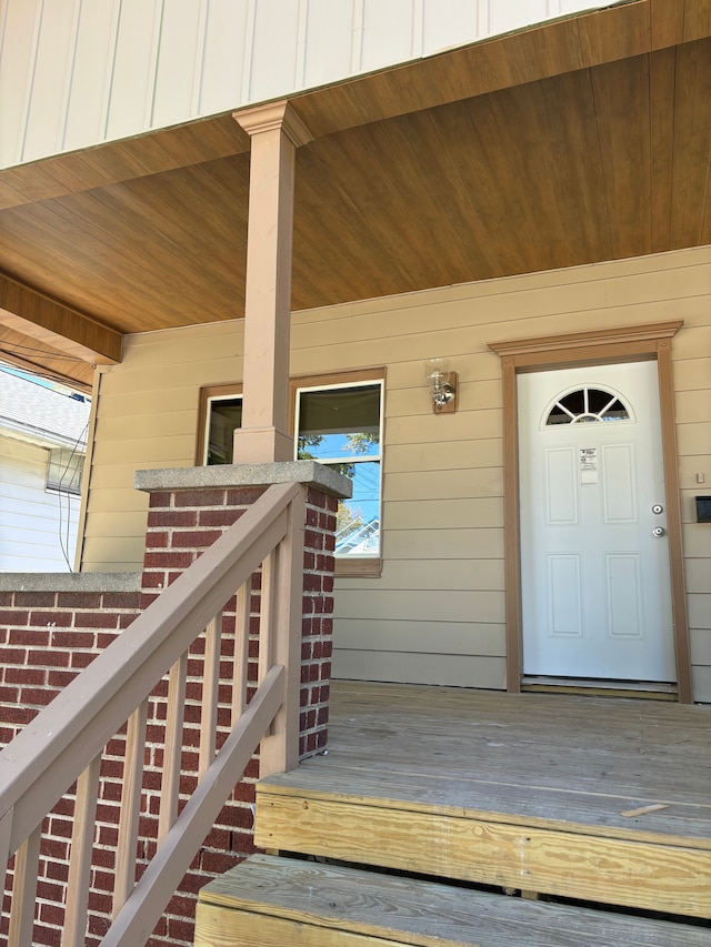 view of exterior entry featuring covered porch, board and batten siding, and brick siding