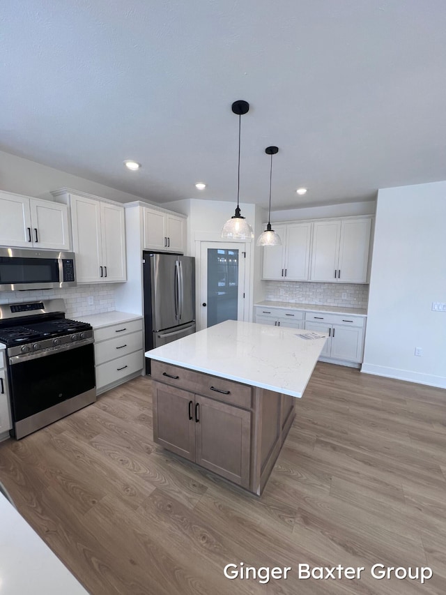 kitchen with appliances with stainless steel finishes, light hardwood / wood-style floors, a kitchen island, and white cabinets