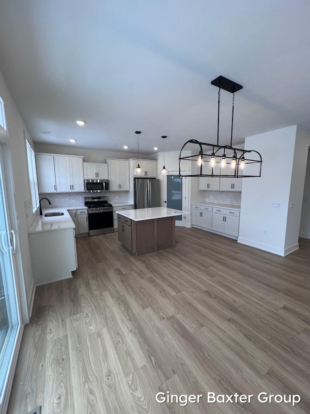 kitchen featuring appliances with stainless steel finishes, decorative light fixtures, white cabinets, decorative backsplash, and a center island