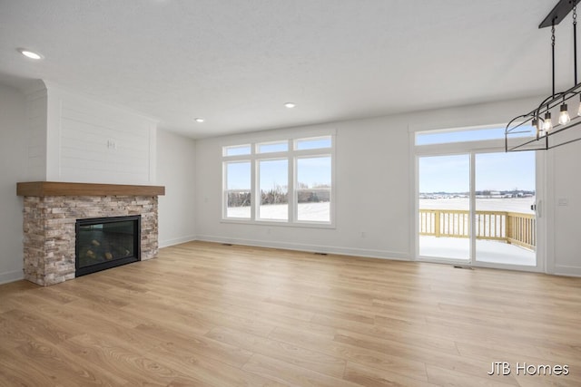 unfurnished living room with a stone fireplace, light wood-style flooring, and baseboards