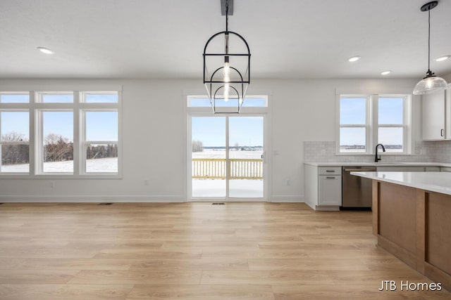 kitchen with light countertops, stainless steel dishwasher, hanging light fixtures, and white cabinetry