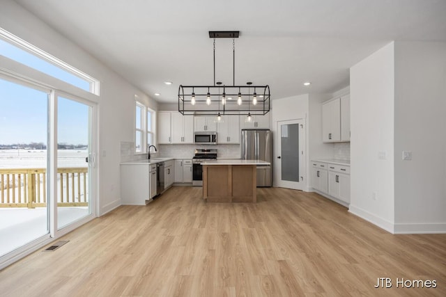 kitchen with a kitchen island, white cabinetry, stainless steel appliances, and light countertops