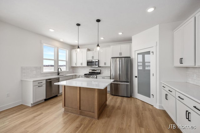 kitchen featuring stainless steel appliances, a sink, a kitchen island, white cabinetry, and light countertops