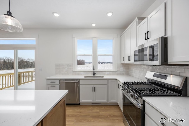 kitchen featuring light wood-style flooring, appliances with stainless steel finishes, hanging light fixtures, white cabinetry, and a sink