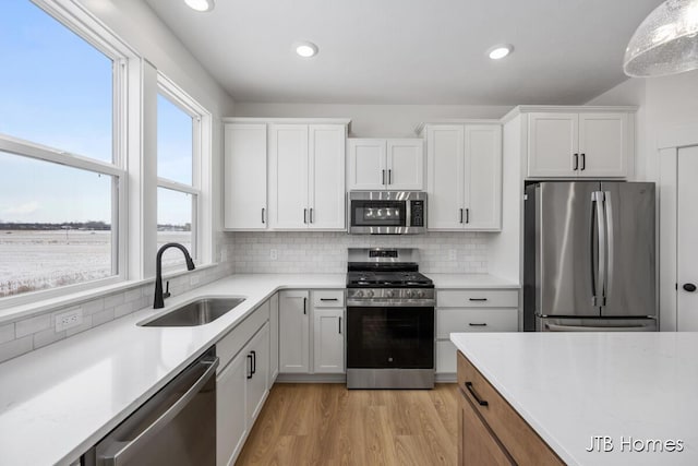 kitchen with stainless steel appliances, a sink, white cabinetry, light wood finished floors, and pendant lighting