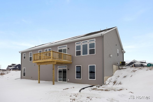 snow covered back of property with central AC and a wooden deck