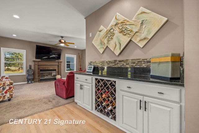 bar featuring ceiling fan, wine cooler, light hardwood / wood-style flooring, dark stone counters, and white cabinets