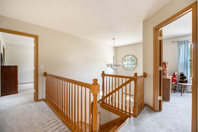 hall featuring light carpet, a textured ceiling, and an inviting chandelier