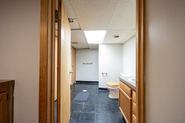 bathroom with a drop ceiling, toilet, and vanity