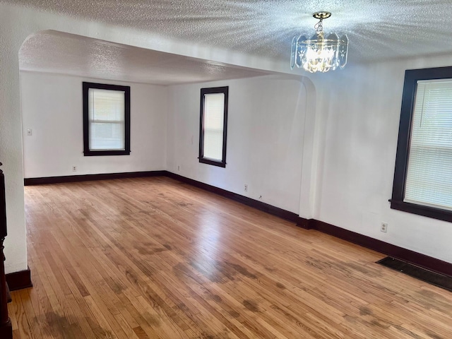 spare room with light wood-type flooring, a textured ceiling, and a notable chandelier