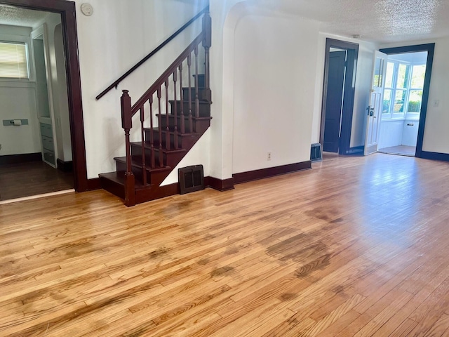 unfurnished living room with light hardwood / wood-style flooring and a textured ceiling