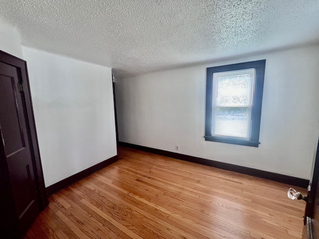 empty room with a textured ceiling and light hardwood / wood-style flooring