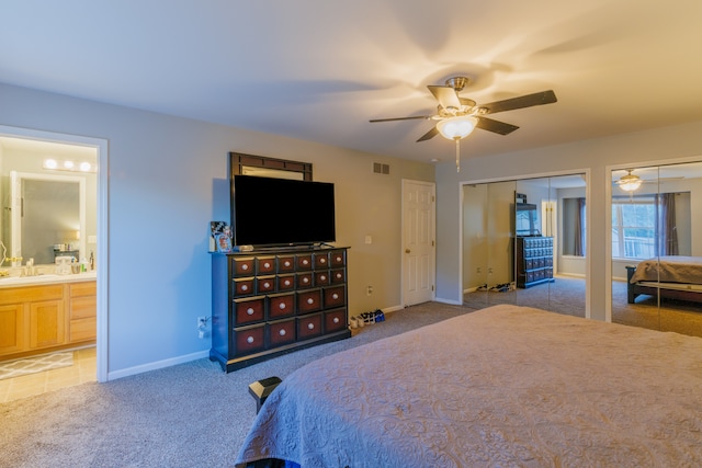 carpeted bedroom featuring ceiling fan, multiple closets, and ensuite bath