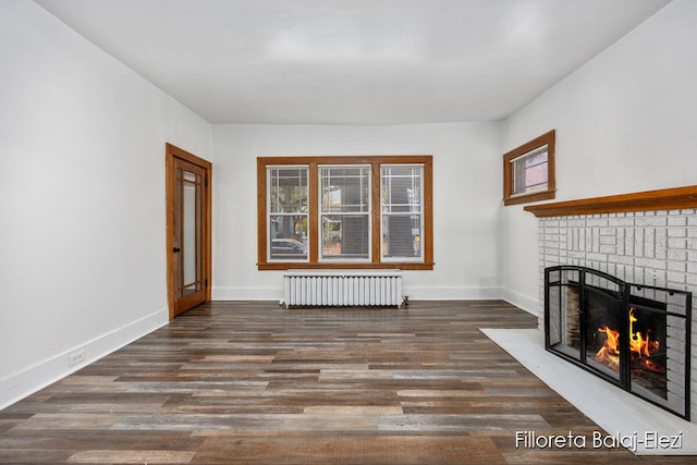 unfurnished living room featuring dark hardwood / wood-style flooring, a brick fireplace, and radiator