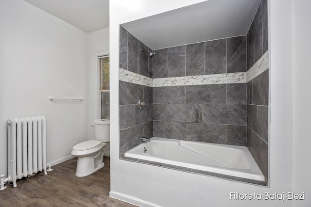 bathroom featuring radiator heating unit, wood-type flooring, tiled shower / bath combo, and toilet