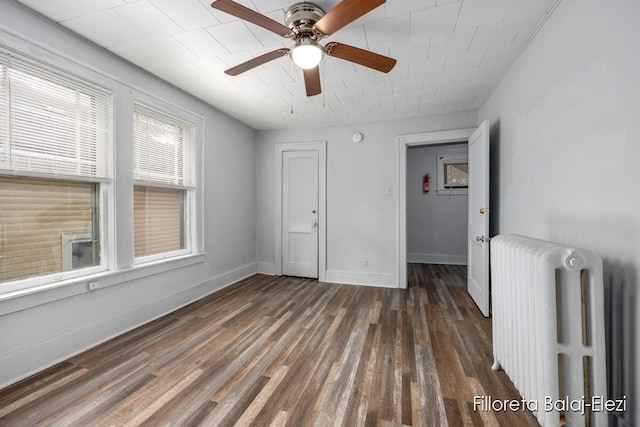 empty room with ceiling fan, radiator heating unit, and dark wood-type flooring