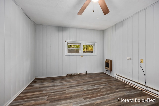 spare room featuring dark hardwood / wood-style flooring, heating unit, baseboard heating, wooden walls, and ceiling fan