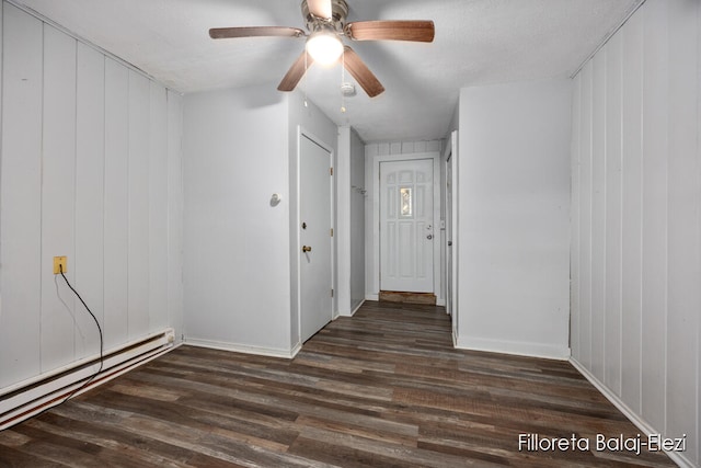 interior space with ceiling fan, a baseboard radiator, dark hardwood / wood-style floors, wood walls, and a textured ceiling