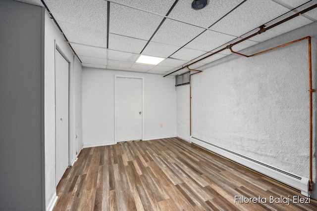 basement with hardwood / wood-style flooring, a drop ceiling, and a baseboard heating unit