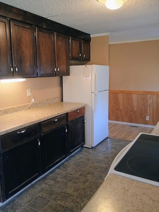 kitchen with stove, white refrigerator, a textured ceiling, and dark brown cabinetry