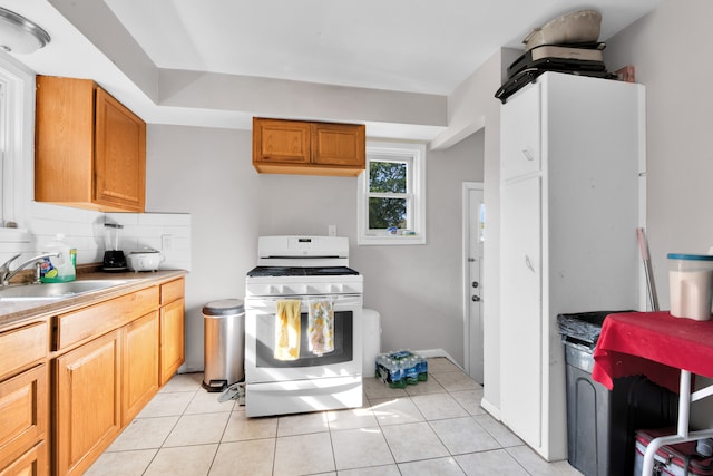 kitchen featuring white range with gas stovetop, sink, light tile patterned floors, and tasteful backsplash