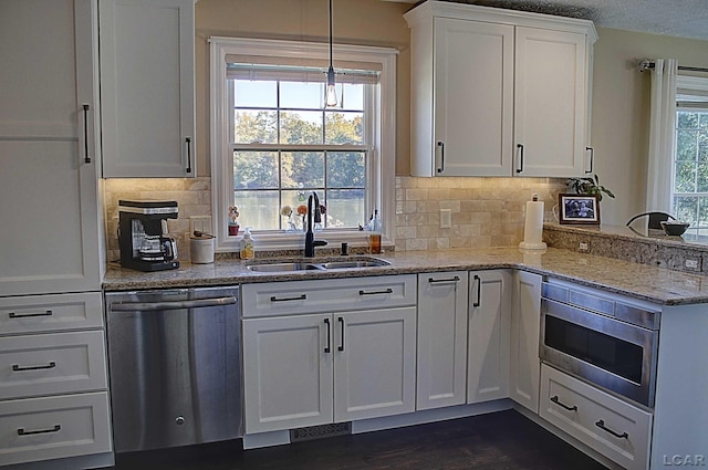 kitchen with sink, white cabinetry, appliances with stainless steel finishes, pendant lighting, and light stone countertops