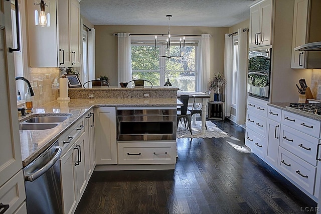 kitchen featuring appliances with stainless steel finishes, white cabinetry, sink, hanging light fixtures, and light stone countertops