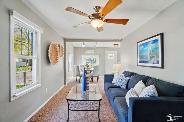 living area featuring ceiling fan, baseboards, and light carpet
